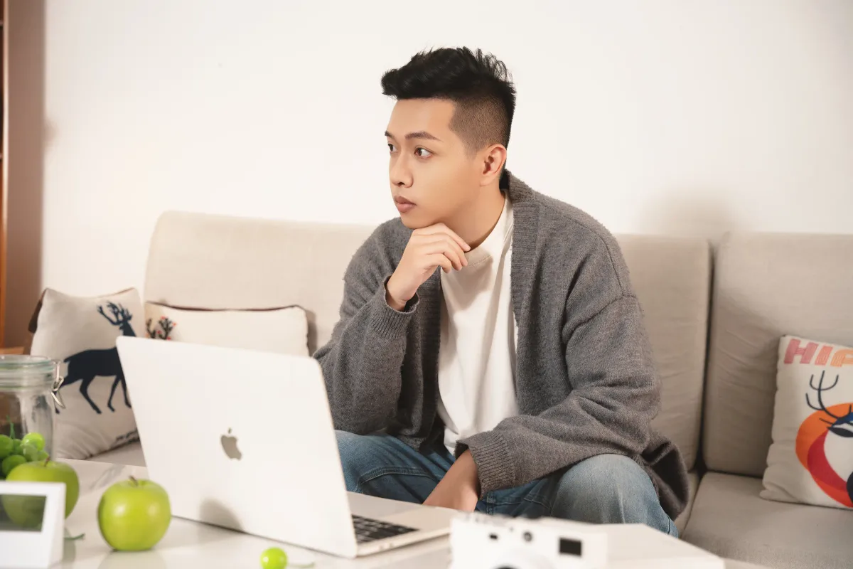 Jimmy 在自然光下坐在沙發前思考，桌上放著 MacBook；既有真實生活肖像