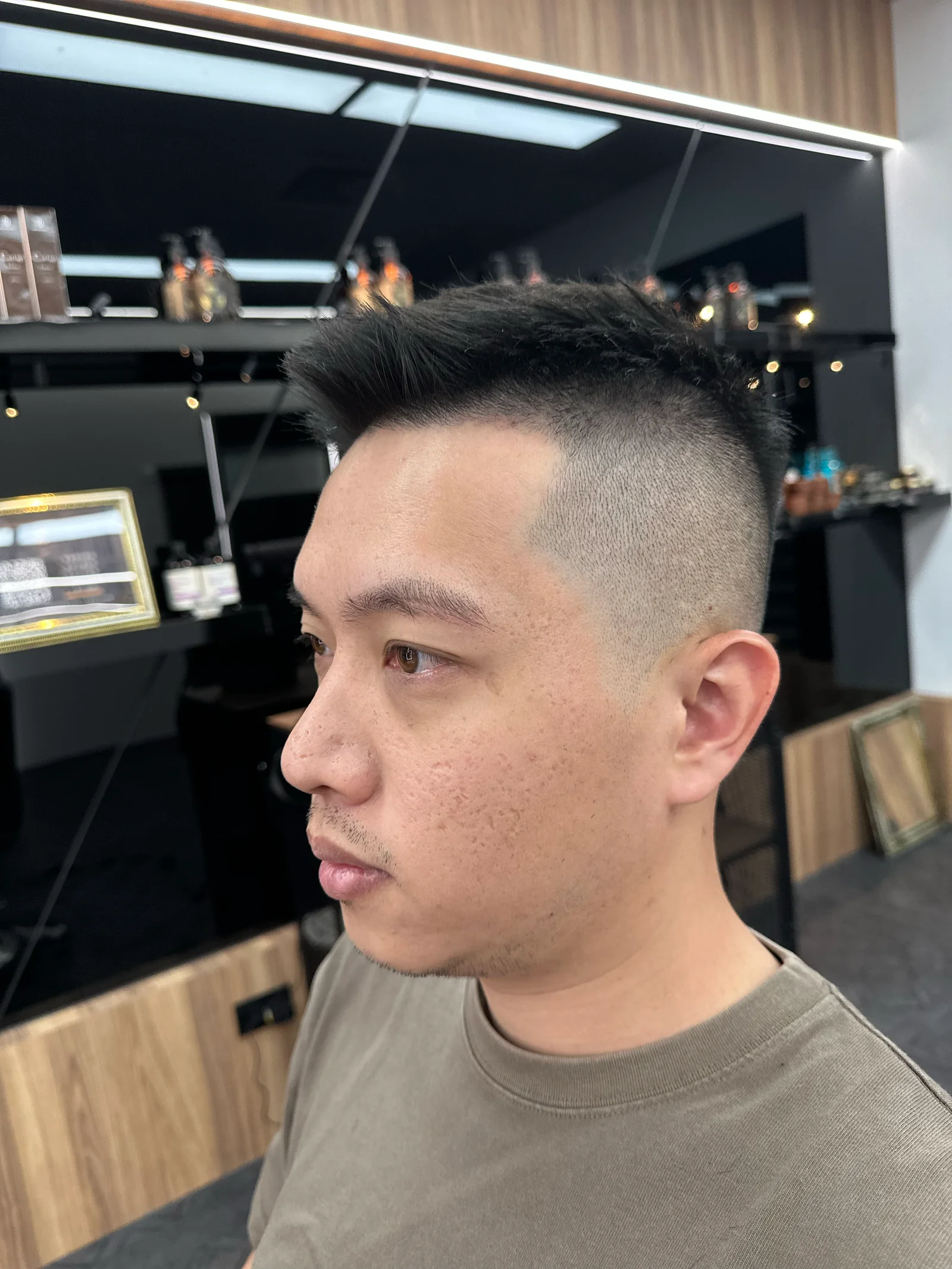 側面特寫，兩側推高收乾淨，頭頂留長往後帶出層次，背景是店內的產品層架