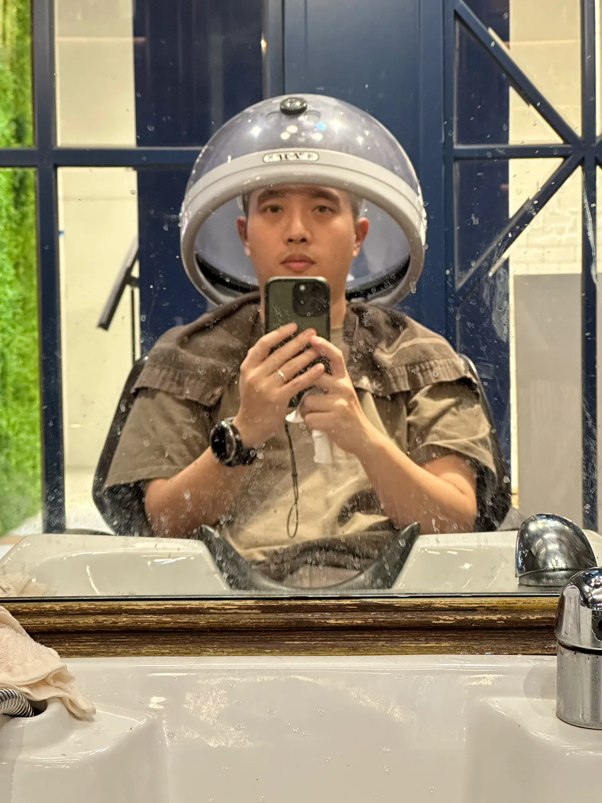 燙髮加熱中，頭上罩著圓形烘罩，身上圍著圍布坐在鏡子前