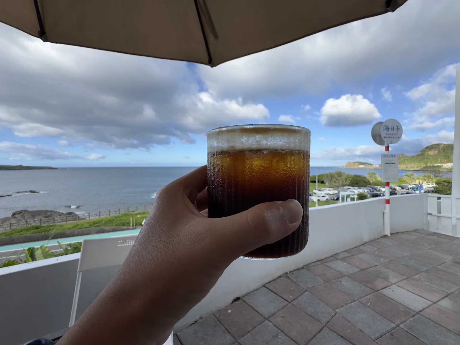 手舉著一杯冰咖啡，背景是北海岸的海與天空
