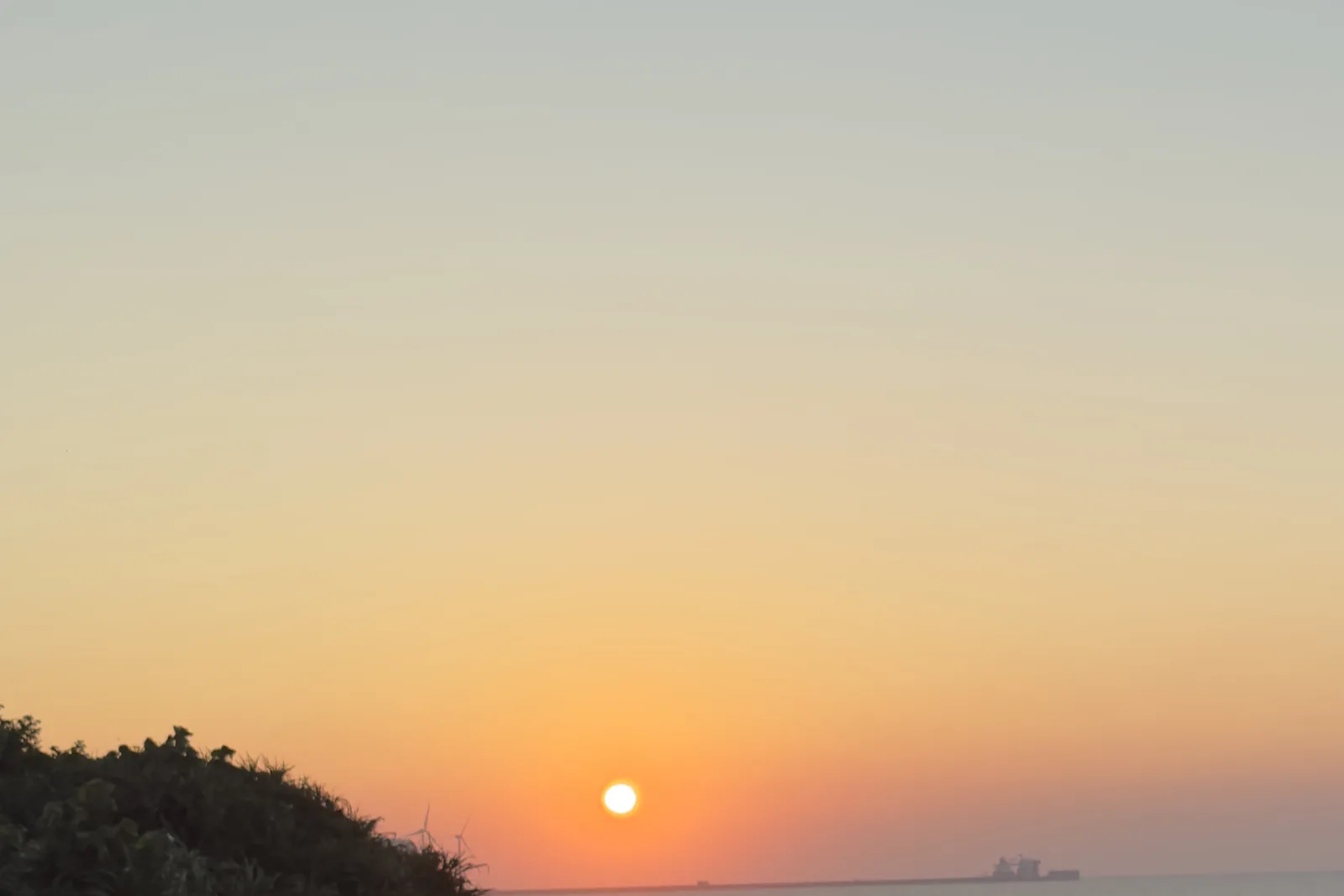 太陽正要沉入海平面，天空從橘色漸層到藍色，遠方有一艘貨輪